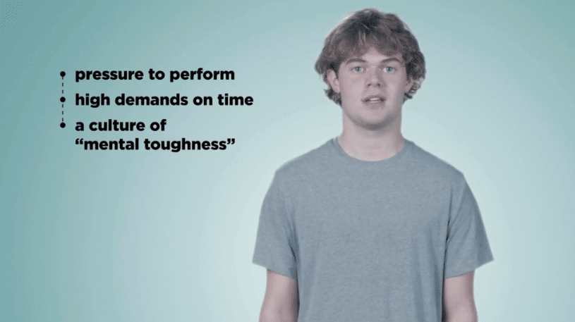 A young man stands in front of a blue background and discusses mental well-being for athletes.