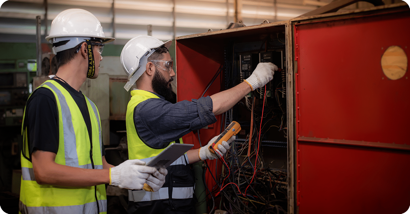 Electrician and engineer in safety uniforms inspecting and maintaining the machine's electrical control cabinet in heavy industrial manufacturer factory.